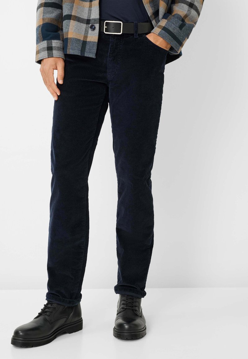 Marineblauwe corduroy broek met een slim fit, voorzien van een klassieke vijf-pocket ontwerp, gedragen met zwarte veterschoenen. De algehele uitstraling is casual.