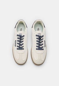 Fehér bőr sportcipők sötétkék fűzővel. Lekerekített orr, textúrált felület, világoskék bélés és gumis talp a tapadásért. A márka logója látható.