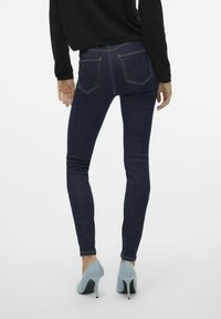 Tanke tamne traperice s zlatnim šavovima, dva stražnja džepa i visokim strukom, uparene s svijetloplavim visokim potpeticama.