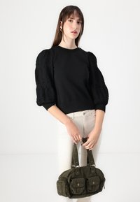 Felpa nera con maniche a sbuffo texture, abbinata a una borsa in velluto a coste verde con diversi scomparti e doppi manici.