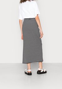 Černobílé pruhované maxi sukně s elastickým pasem, doplněná bílými sandály s tlustou podrážkou a nastavitelnými popruhy.