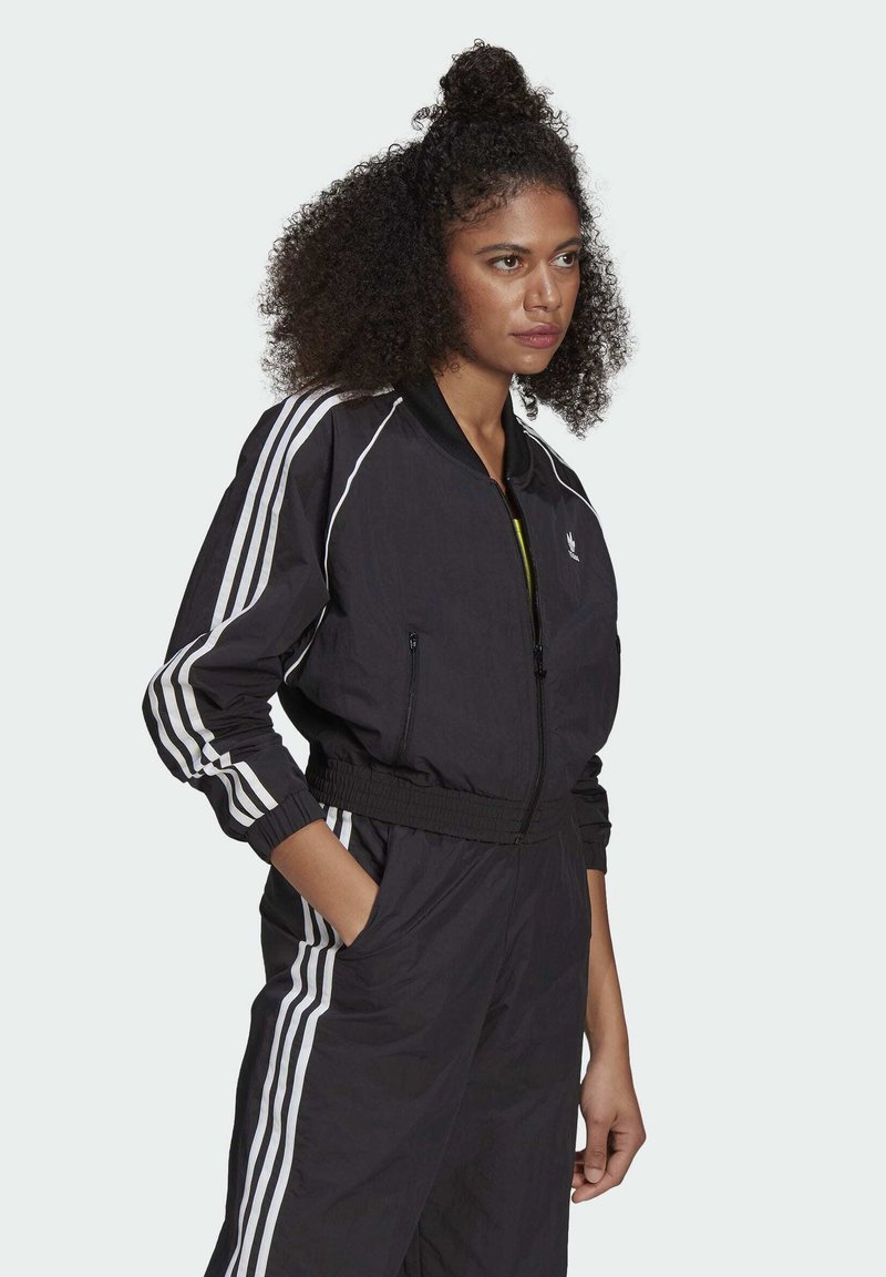 Giacca bomber nera con strisce bianche sulle maniche, chiusura con zip, polsini e vita a costine. Realizzata in tessuto leggero e testurizzato.