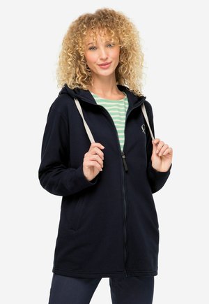 Felpa con zip navy e cappuccio, con laccetti crema, tasche laterali e polsini a coste. Modello che indossa una maglietta a righe sotto.