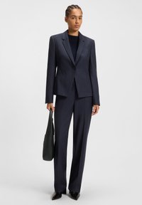 Laiva sininen pinstripe puku, jossa on istuva bleiseri ja suorat housut. Ominaisuuksiin kuuluu yksi nappi, lovet lapelit ja sileä rakenne.