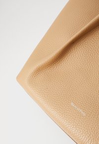 Tanskleurige leren clutch met een gestructureerd oppervlak, voorzien van een subtiel in wit geperst logo. Ronde hoeken met gestikte details.