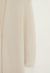 Beige neuletakki, joka on valmistettu pehmeästä neulomateriaalista, rento istuvuus, avonainen etuosa ja resorikätiset. Hienovarainen tekstuuri kauttaaltaan.