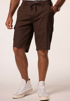 Braune Cargo-Shorts mit elastischem Bund, Kordelzug und seitlichen Taschen, kombiniert mit weißen High-Top-Sneakers vor einem hellen Hintergrund.