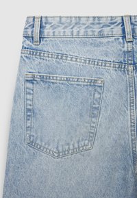 Tessuto di denim azzurro chiaro con una tasca posteriore, cuciture visibili e una trama distintiva con un motivo sbiadito.