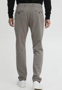 Pantalons gris sur mesure avec une texture subtile, dotés de deux poches arrière avec boutons et d'un design à jambe droite. Portés avec des baskets blanches.
