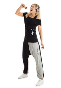 Black off-shoulder top paired with relaxed-fit, color-blocked gray and black sweatpants. White sneakers; model wears headphones.
