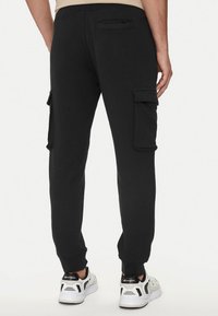 Pantaloni cargo neri in cotone con tasche cargo laterali, gamba affusolata e polsini a costina. Realizzati in un tessuto morbido, con una superficie liscia.