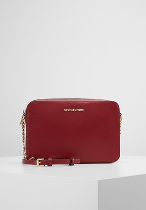 Rode Michael Kors leren crossbodytas met gouden ketting en logo, rechthoekige vorm, ritssluiting en verstelbare riem op een witte ondergrond.