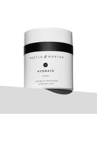 Pot de crème hydratante cylindrique blanc avec un couvercle noir et du texte. L'étiquette indique "Pestle & Mortar Hydrate Crème Hydratante Légère" en police noire.