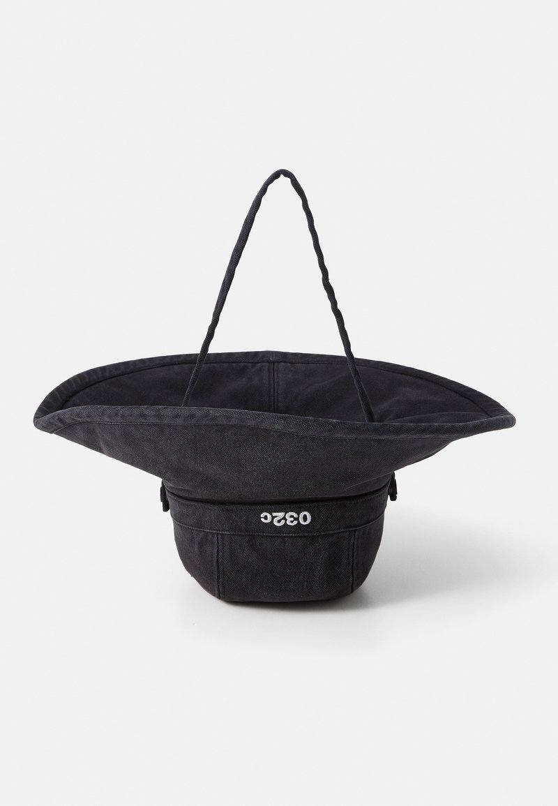 Black canvas tote bag with a wide, flared top, thick twisted handles, and a zippered bottom compartment featuring a logo.