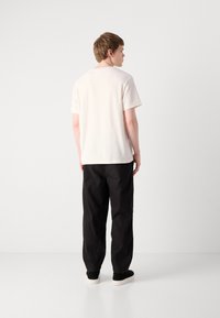 Ljust beige kortärmad t-shirt i mjuk textur, kombinerad med lösa svarta byxor och svarta skor med vita sulor. Minimalistisk design, neutrala färger.