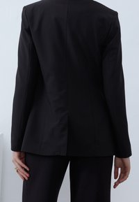 Zwarte op maat gemaakte blazer met lange mouwen, gestructureerde vorm en een enkele rugopening; stijlvolle stof met een gladde textuur, zonder zichtbare patronen.