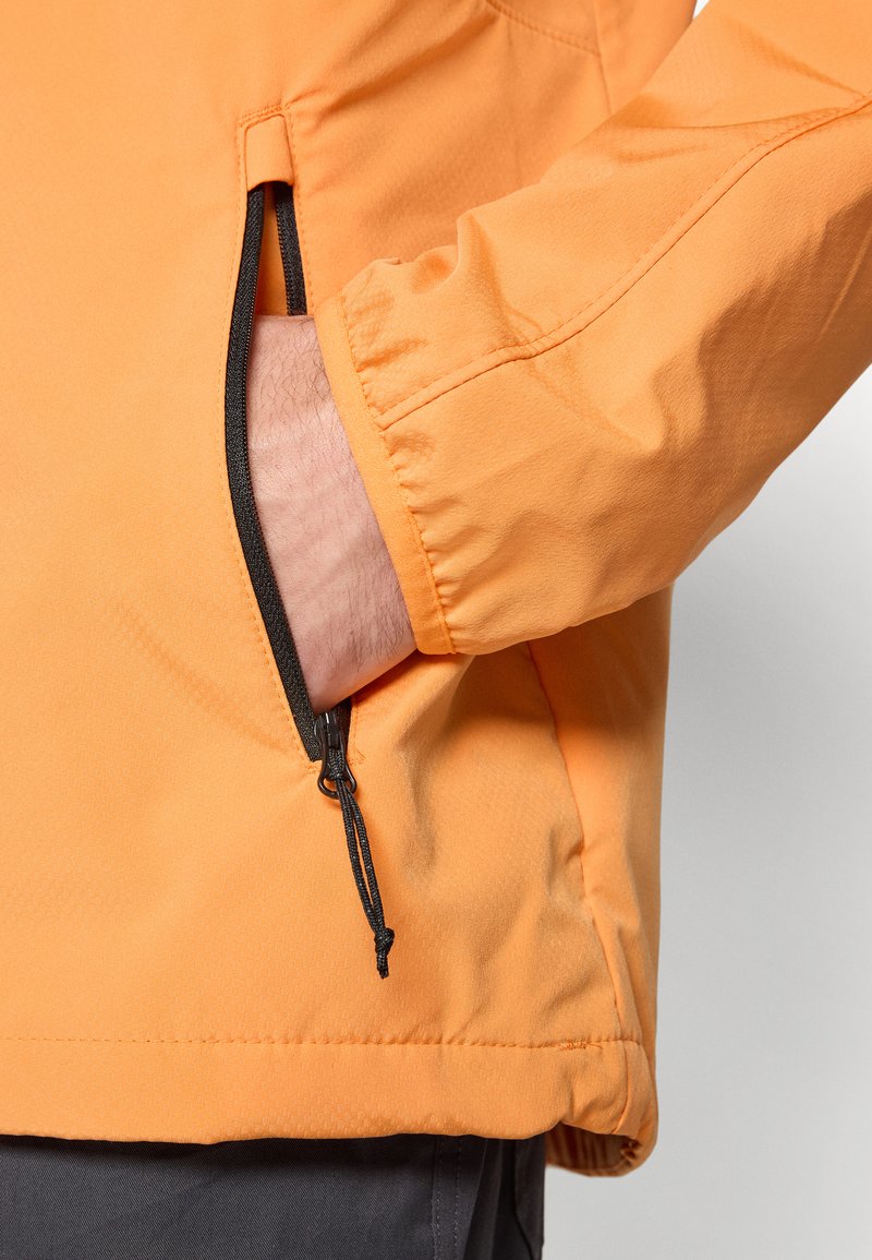 Pomarańczowa wodoodporna kurtka o smukłym kroju, z elastycznymi mankietami i kieszenią na zamek. Posiada subtelną teksturę i ściągacz u dołu.