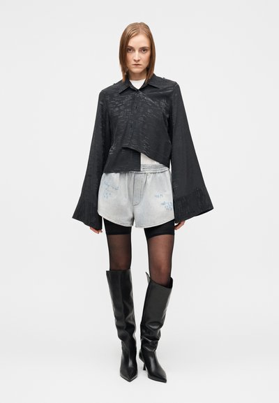 Μαύρο κοντό σακάκι με φαρδιά μανίκια, υφασμάτινη υφή. Ανοιχτό γκρι σορτς από τζιν με μπλε λεπτομέρειες. Ψηλές μαύρες μυτερές μπότες.