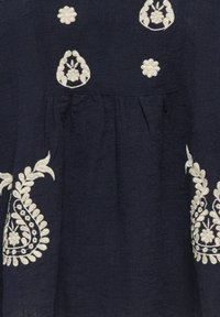 Temno modro blago z belo vezenino cvetov in listov ter gubami pod izvezenimi detajli.