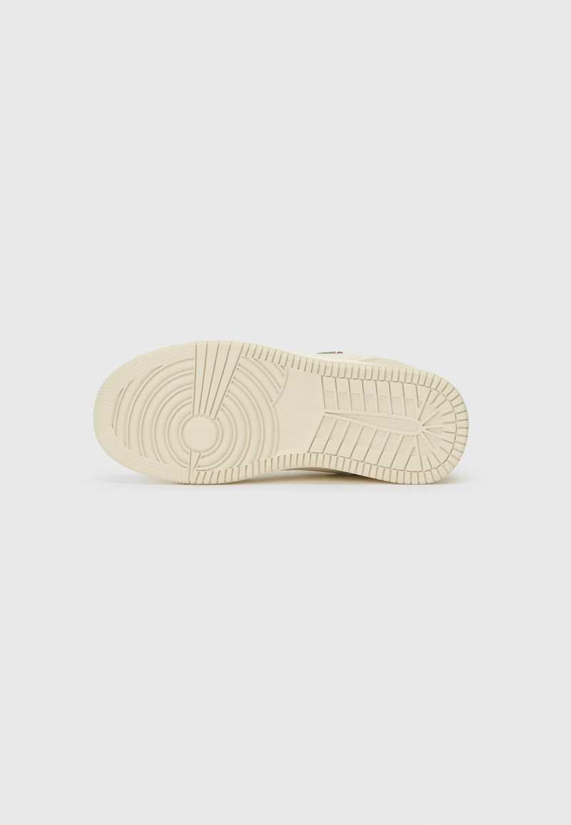 Semelle de sneaker beige clair avec un motif texturé, présentant des designs circulaires et linéaires pour l'adhérence. Matériau lisse et forme arrondie.