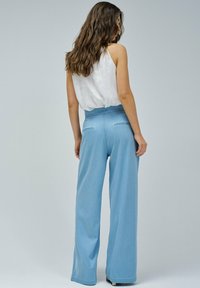 Pantalons large bleu clair à taille haute, en denim, dotés de poches arrière et d'une texture lisse. Portés avec un haut blanc.