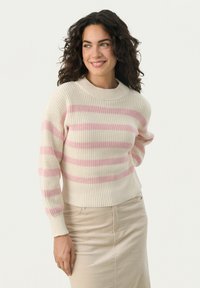 Helles beiges Sweatshirt mit rosa horizontalen Streifen, gerippter Textur und rundem Ausschnitt. Kombiniert mit einem beigen Rock.