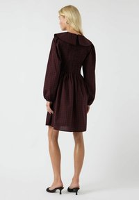 Abito in bordeaux con motivo a quadri, corpino arricciato e colletto oversize. Maniche lunghe con polsini arricciati.