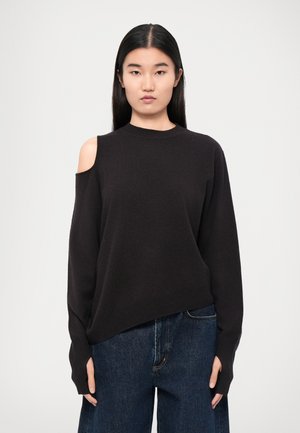 Svart genser med høy hals, åpne skulderdetaljer og lange ermer. Myk tekstur og avslappet passform. Kombinert med mørke jeans.