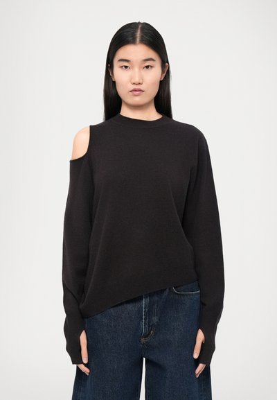 Suéter negro con un cuello alto, detalle de hombro descubierto y mangas largas. Textura suave y corte relajado. Combinado con jeans de mezclilla oscuros.