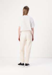 Vit kortärmad t-shirt, krämfärgade sweatpants med elastisk midja och bakficka, tillsammans med svarta sneakers på en vit bakgrund.