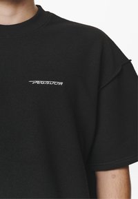T-shirt nera oversize in tessuto morbido con colletto a girocollo a costine; presenta il logo "PEGADOR" ricamato in bianco sul lato sinistro del petto.