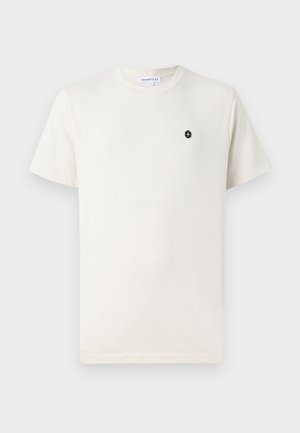 Kreemivärviline puuvillane T-särk lühikeste varrukatega, ümmargune kaelus ja väike must kuuekülgne logo vasakul rinnapiiril. Sile tekstuur.