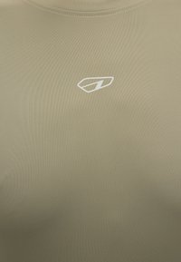 Μπεζ ύφασμα με μικρό λευκό γεωμετρικό λογότυπο κεντραρισμένο κάτω από το λαιμόκοψη, ραμμένο κολάρο ορατό στο επάνω μέρος.