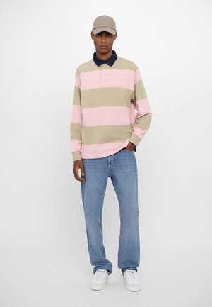 Langærmet polo i beige, pink og marineblå striber med krave, parret med lyseblå jeans og hvide sneakers. Grå kasket fuldender outfittet.
