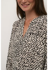 Blouse noire et crème avec un col en V, ornée d'un motif à pois. Le tissu semble léger avec une texture lisse et des manches amples.