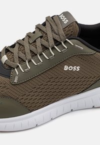 Baskets en textile marron avec un design en maille, comprenant des accents gris et une semelle blanche. Logo "BOSS" affiché sur le côté latéral. Lacets plats.