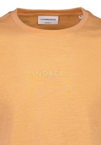 T-shirt a maniche corte in cotone morbido e leggero color arancione chiaro, con logo "LINDBERGH" in rilievo sulla parte anteriore, colletto rotondo e una texture liscia.