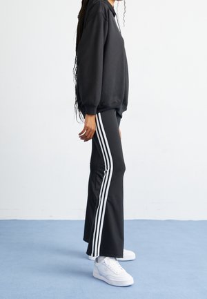Black sweatshirt with a relaxed fit, paired with black pants featuring three white vertical stripes along the sides. White sneakers complete the look.
