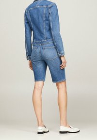 Jeansjacka och shorts-set i medelblått. Fitted design med synliga sömmar, två bakfickor och klassisk krage. Vita skor ingår.