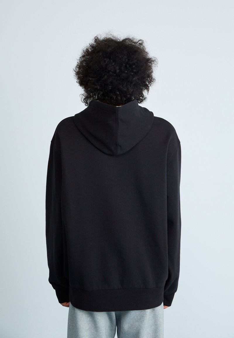 Schwarze Kapuzenjacke mit lockerer Passform, mit Kängurutasche, gerippten Bündchen und einer weichen Textur. Ansicht von hinten.