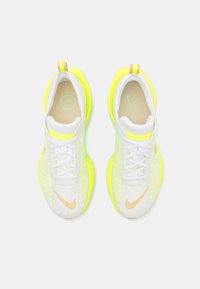 Baskets de course blanches avec des accents jaune fluo, tige en mesh, semelle texturée et fermeture à lacets. Présente un petit logo près du talon.