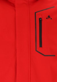 Rote Jacke mit glatter Textur, ausgestattet mit einer schwarzen Reißverschlusstasche und geometrischen schwarzen Akzenten. Enthält ein kleines Logo in der oberen Ecke.