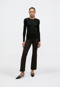 Haut noir à manches longues et pantalon évasé marron, assortis à des chaussures noires à bouts pointus. La tenue présente une coupe ajustée et une texture lisse.