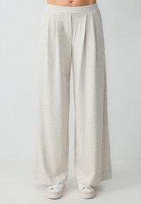 Pantalons à jambes larges en beige clair, fabriqués dans un tissu doux avec une texture subtile. Présente un devant plissé et une taille élastique assortie.