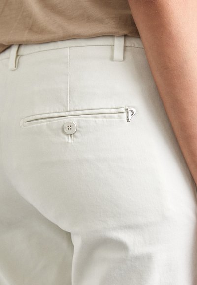 Pantaloni albi din bumbac, cu un buzunar la spate prevăzut cu un închizător cu buton și un mic accent argintiu. Țesătura are o textură netedă.
