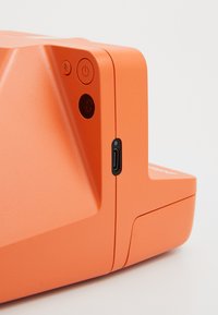Narancssárga elektronikus eszköz, texturált felülettel, amelyen található egy bekapcsoló gomb, egy jelzőfény és egy USB-C port az oldalon.