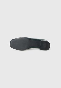Suola di una scarpa formale nera con tacco antiscivolo texturizzato e suola anteriore liscia, vista dal basso su uno sfondo bianco.