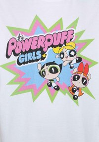 Hvit t-skjorte med fargerik tegneserieillustrasjon av tre karakterer. Teksten sier "Powerpuff Girls" med livlige grønne og rosa aksenter.
