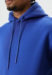 Blue cotton hoodie with drawstrings. The fabric is smooth with a slight sheen, featuring a kangaroo pocket and ribbed cuffs.