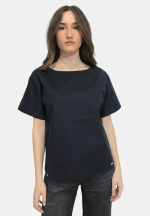Top blu navy a maniche corte con scollatura rotonda, realizzato in tessuto liscio. Abbinato a jeans scuri e testurizzati con dettagli di branding minimi.